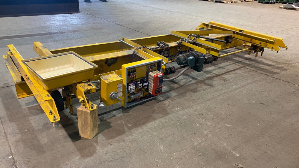 Overhead crane modernization in progress, showing a disassembled yellow crane bridge with updated control panel components, motor, and electrical wiring exposed on a shop floor.