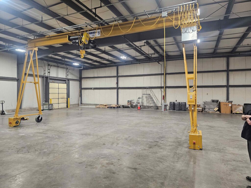5-ton motorized gantry crane with electric hoist, powered travel drive, and festooned pendant controls installed in an industrial facility.